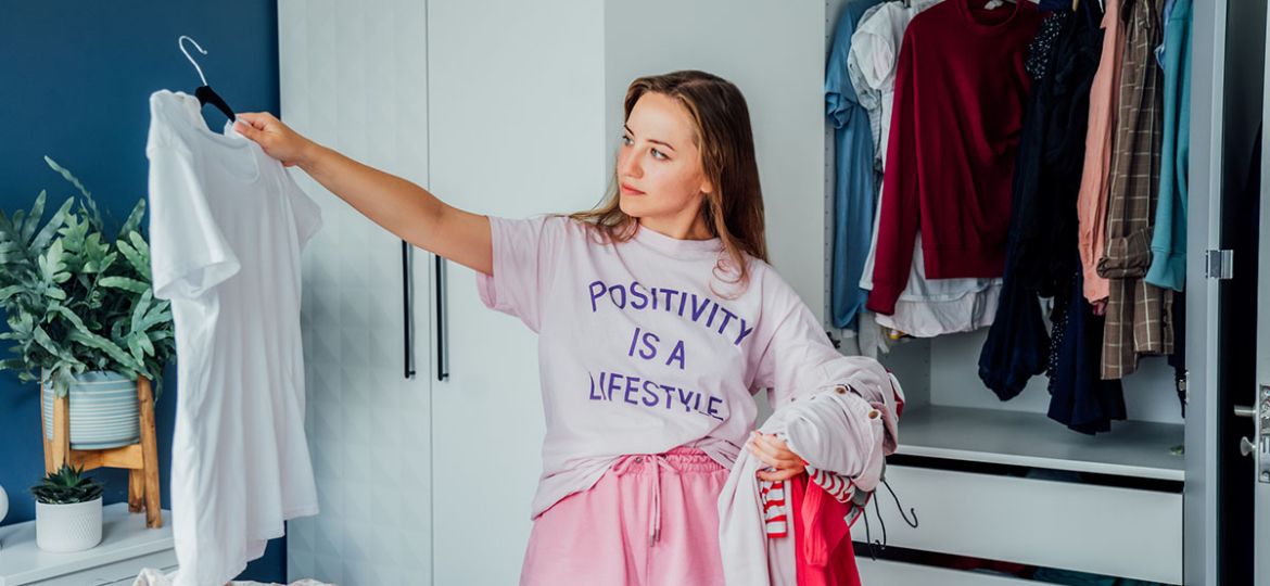 Woman selecting clothes from her wardrobe for donating to a Charity shop. Decluttering, Sorting clothes and Cleaning Up. Reuse, second-hand concept. Conscious consumer, sustainable lifestyle.