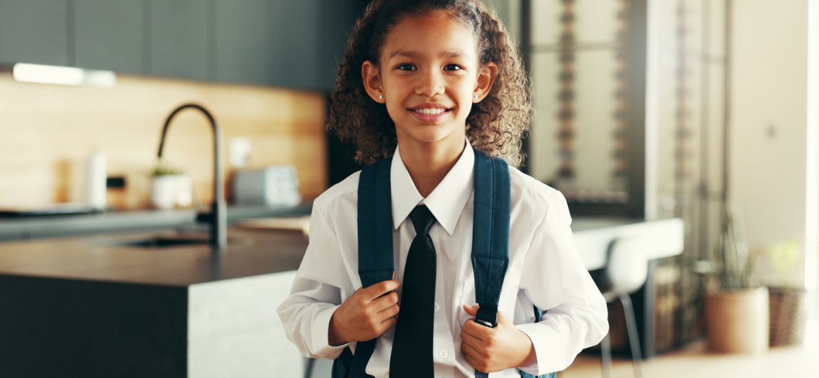 Portrait, happy kid and student with school uniform in home for learning, education or study in kitchen. Face, smile or girl child in elementary for first day, growth or ready for knowledge in Brazil