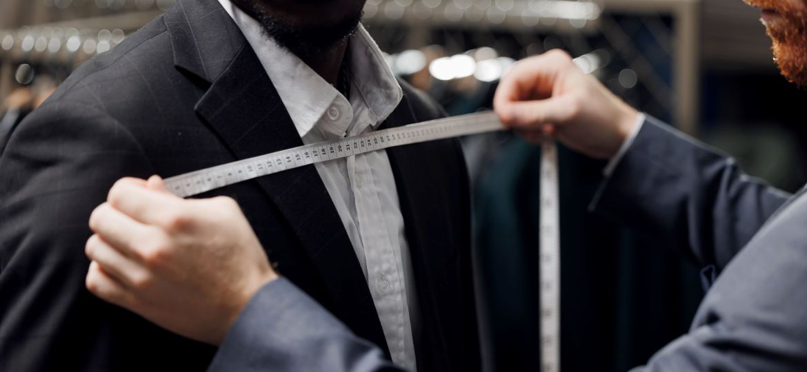 Professional tailor measuring client African American man for bespoke suit in luxury designer atelier
